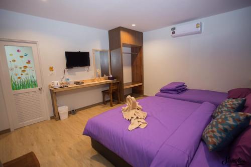 a bedroom with two beds with purple sheets and a desk at Green Two Resort in Chanthaburi