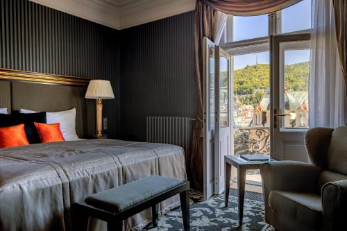 a bedroom with a bed and a chair and a window at Grandhotel Pupp in Karlovy Vary