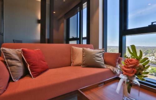 an orange couch with pillows in a room with windows at Box Hill Central Sky One Apartment in Box Hill