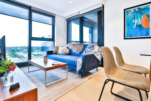 a living room with a blue couch and large windows at Box Hill Central Sky One Apartment in Box Hill