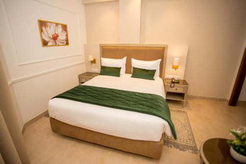 a bedroom with a large bed with two green pillows at HOTEL PALAIS ROYAL in Sfax