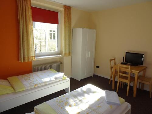 a bedroom with two beds and a desk and a window at Gästehaus Grupello in Düsseldorf