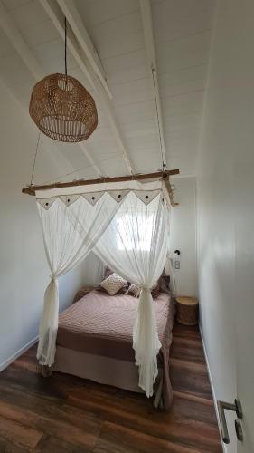 1 dormitorio con cama con dosel y cortinas blancas en Chez Lauvineth, en Sainte-Rose