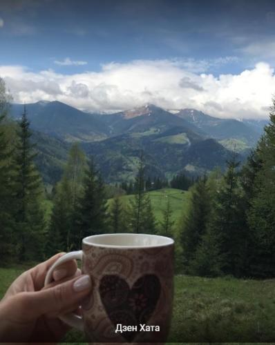 a person holding a coffee cup with a view of mountains at Дзен Хата in Dzembronia