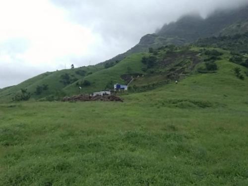 a green hill with a house on top of it at Jandyal Farm House in Malshej Ghat