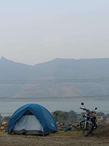 a blue tent and a motorcycle parked next to a lake at Jandyal Farm House in Malshej Ghat