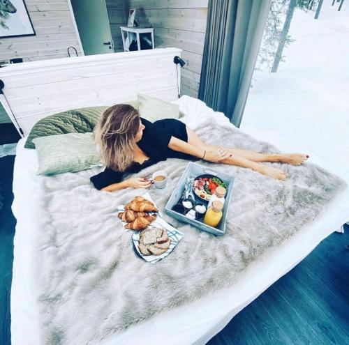 a woman laying on a bed with a tray of food at Arctic Skylight Lodge in Äkäslompolo