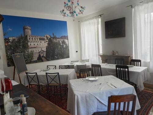 un ristorante con tavoli e sedie bianchi e un dipinto sul muro di B&B La Loggia Del Castello a Trento