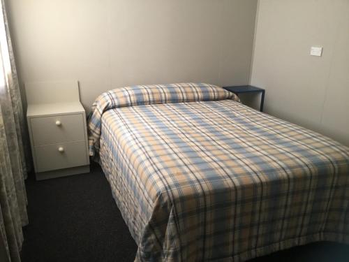 Dormitorio pequeño con cama con manta a cuadros en Mountains Edge Cabins, en Monowai