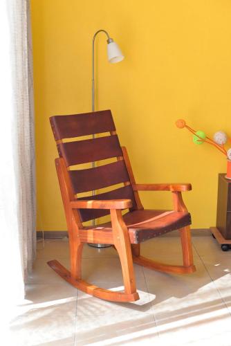a wooden rocking chair sitting in front of a yellow wall at Supercostarica in Grecia