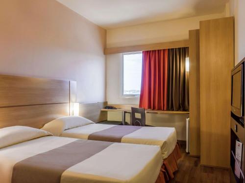 a hotel room with two beds and a window at ibis Jaboticabal in Jaboticabal