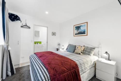 a white bedroom with a bed with a red blanket at Bellbird Cottage - Lake Taupo Bach in Waitahanui