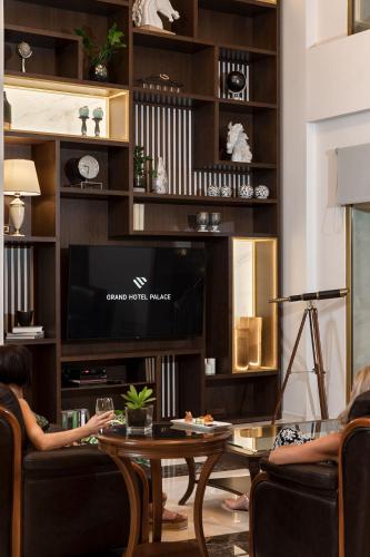 two people sitting in chairs in a living room with a television at Grand Hotel Palace in Thessaloniki