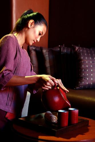 a woman is holding a tea pot on a table at The BARAI by Hyatt in Hua Hin