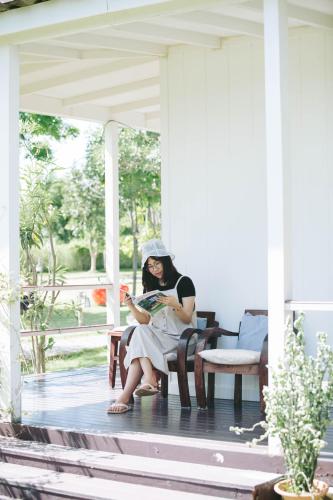 a woman sitting on a porch reading a book at Terrua Main Ten Villa Garden in Suan Phung