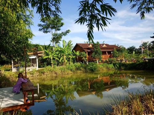 a woman sitting on a bench next to a river at เรือนไทยใจสุขเอ๋ย in Ban Bang Wa