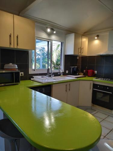 a large kitchen with a green table in it at Lounge des hauts, 3 maisons à L'étang-Salé avec vue sur l'Océan indien et la forêt in Étang-Salé