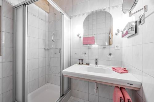a white bathroom with a sink and a shower at Hotel Nevada in Samnaun