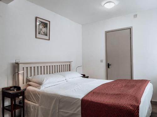 a white bedroom with a bed with a red blanket at The Blenheim Buttery in Woodstock