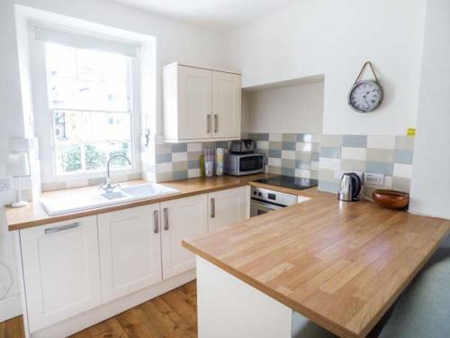 a kitchen with white cabinets and a clock on the wall at Bridge End Cottage in Carnforth