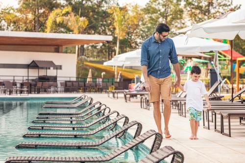 a man and a child walking by a swimming pool at Novotel Itu Terras de São José Golf & Resort in Itu