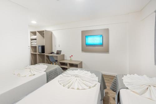 a white room with two beds and a tv at Prime Hotel Ponta Porã in Ponta Porã