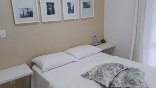a white bed with a pillow and pictures on the wall at Apartamento na Riviera de São Lourenço in Riviera de São Lourenço