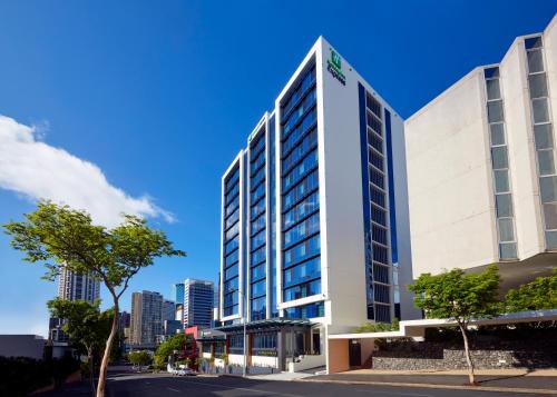 a tall white building in front of a city at Holiday Inn Express Brisbane Central by IHG in Brisbane