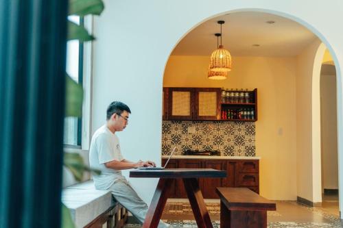 Ein Mann, der mit einem Laptop an einem Tisch sitzt. in der Unterkunft Lacasa Homestay in Hue