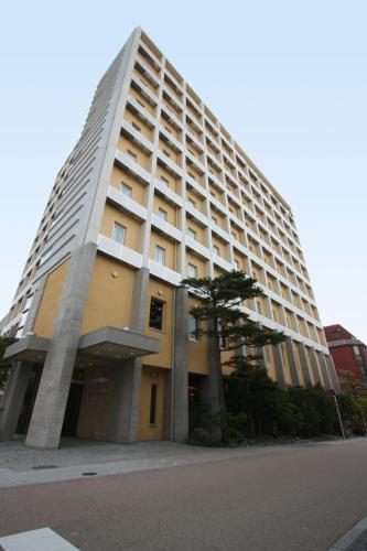 a tall building with a tree in front of it at Uozu Manten Hotel Ekimae in Uozu