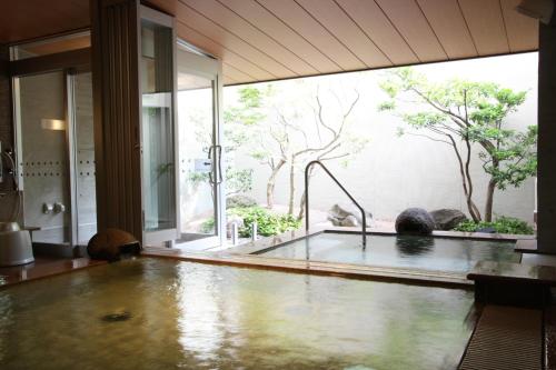 a bathtub in a room with a large window at Uozu Manten Hotel Ekimae in Uozu