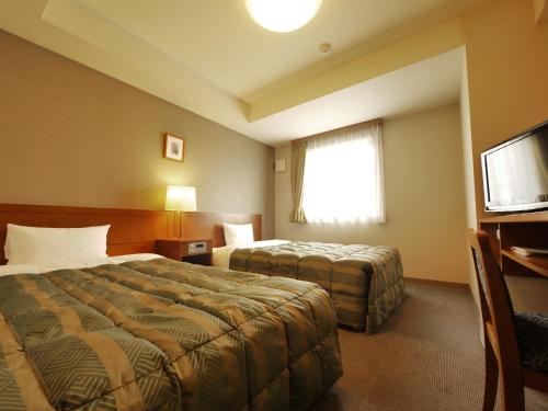 a hotel room with two beds and a television at Hotel Route-Inn Honjo Ekiminami in Honjo