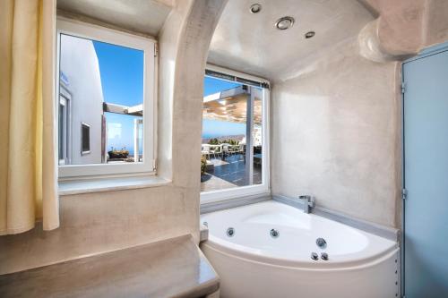 baño con bañera, aseo y ventana en Katerina's Castle - Caldera Cave Hotel, en Imerovigli