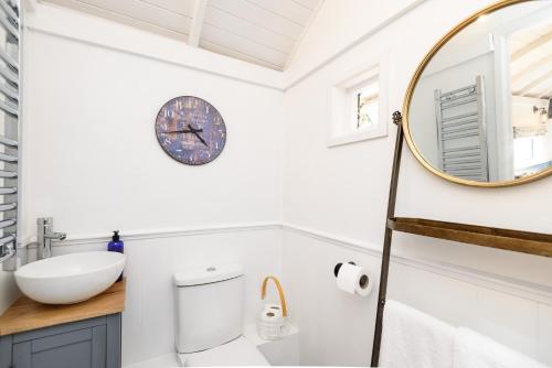 La salle de bains est pourvue d'un lavabo et d'une horloge murale. dans l'établissement Penlea Retreat Luxury Coastal Shepherds Hut 5 Minute Walk to Pubs and Village, à Polperro