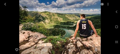 a man sitting on the edge of a cliff overlooking a river at Markove kolibe 2, Uvac in Sjenica