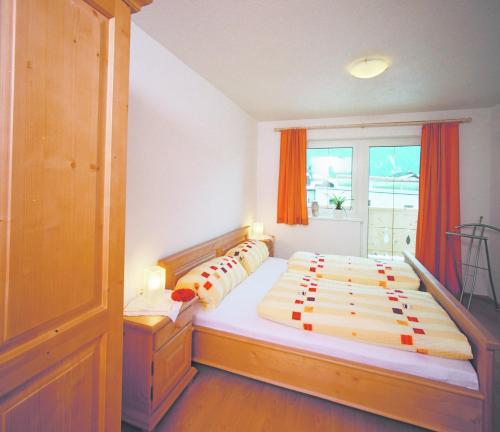 ein Schlafzimmer mit einem großen Bett mit orangefarbenen Vorhängen und einem Fenster in der Unterkunft Anton´s Appartements in Oetz