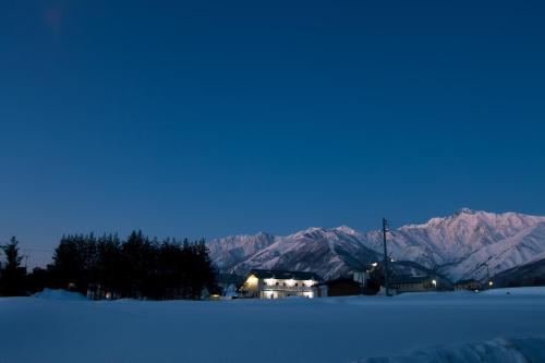 a house in the snow with mountains in the background at Pals Inn Raicho in Hakuba