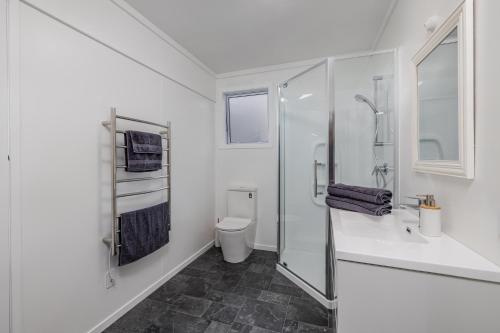 a white bathroom with a shower and a toilet at Waterfront Beach House - Paihia Holiday Home in Paihia
