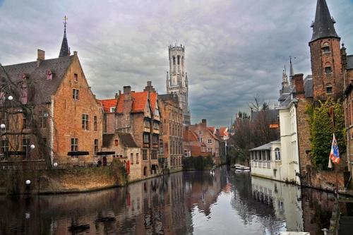 a river in a city with buildings and a cathedral at Hotel Loreto in Bruges