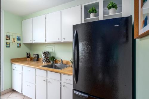 a black refrigerator in a kitchen with white cabinets at Top Floor Ocean Views Condo in Kihei