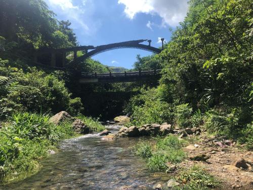 a bridge over a river with a dirt road at Jiufen Gourd Stone TreeHouse 137 in Ruifang