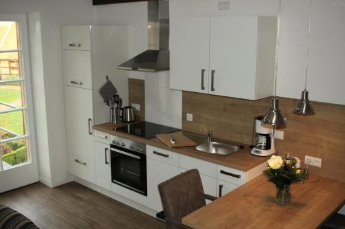 cocina con armarios blancos y mesa de madera en Ferienwohnung Lodberger Scheunencafe, en Löningen