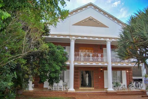 a red brick house with a balcony and trees at Hamilton Urban Farm Guest House in Pietermaritzburg