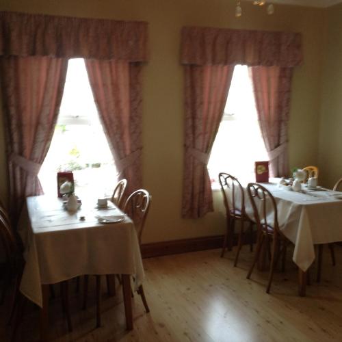 two tables and chairs in a room with windows at Deerpark Manor Bed and Breakfast in Swinford