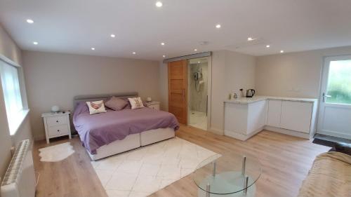 a bedroom with a bed with purple sheets and a kitchen at The Garden Room, 1 Heath Cottage in Knutsford