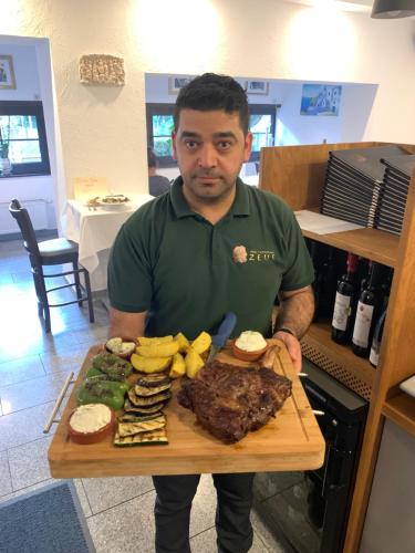 a man holding a cutting board with a plate of food at Hotel und Restaurant Zeus in Wolfsburg