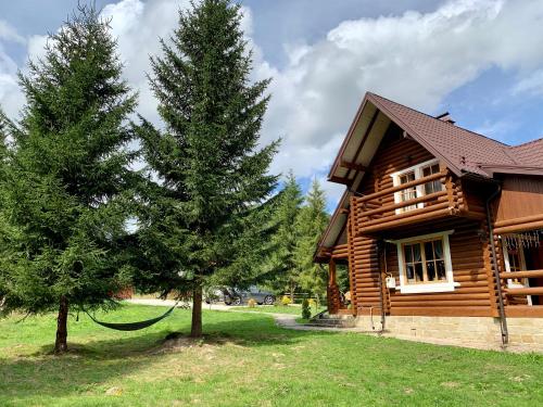 ein Blockhaus mit einem Baum davor in der Unterkunft Котедж Гута in Guta