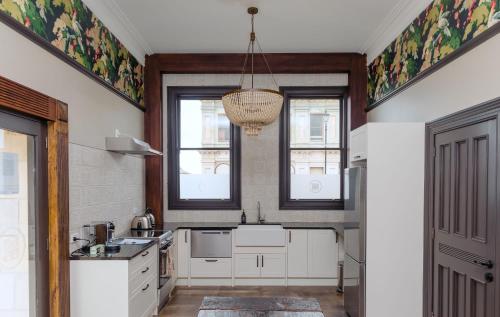a kitchen with white cabinets and windows and a chandelier at The Old Confectionery in Oamaru