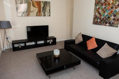 ein Wohnzimmer mit einem schwarzen Sofa und einem Flachbild-TV in der Unterkunft South Shields Central in South Shields