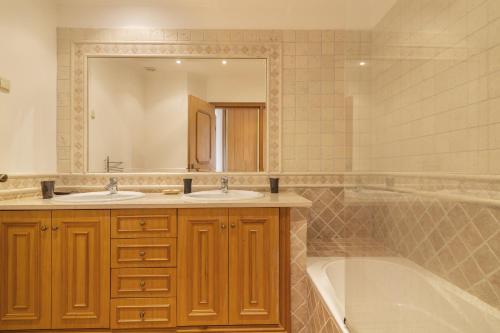 een badkamer met 2 wastafels, een bad en een spiegel bij Seagull House in Quinta do Lago